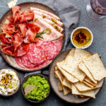 Antipasto. Meat platter, chips and sauces, red wine on gray background